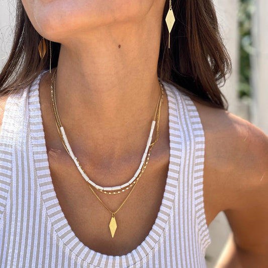 אישה לובשת סט שרשראות זהב עם חרוזים לבנים ותליון מעוין, בלוק קיץ קליל עם גופיית פסים