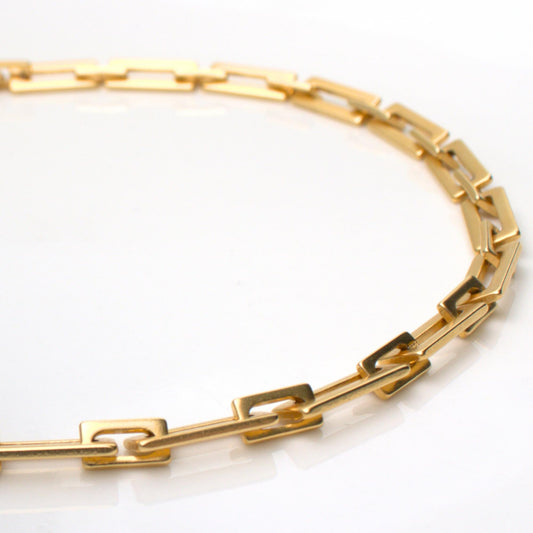 שרשרת זהב עבה בעיצוב חוליות מלבניות, מונחת על רקע לבן, צילום תקריב מקצועי