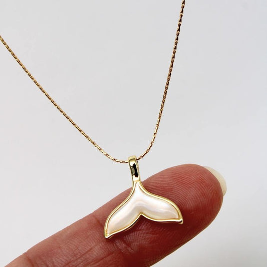 תליון סנפיר זהב מונח על אצבע להמחשת הגודל.