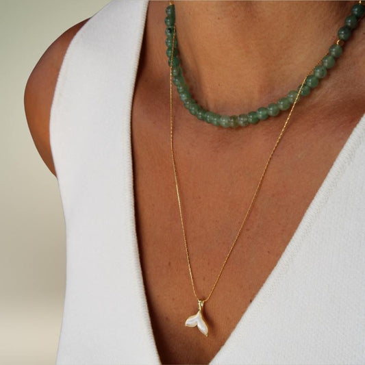 שרשרת סנפיר זהב משולבת עם שרשרת אבני חן ירוקות על צוואר.